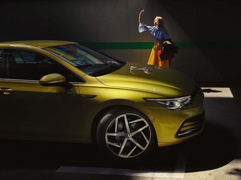Yellow car with rims in focus, woman standing behind it