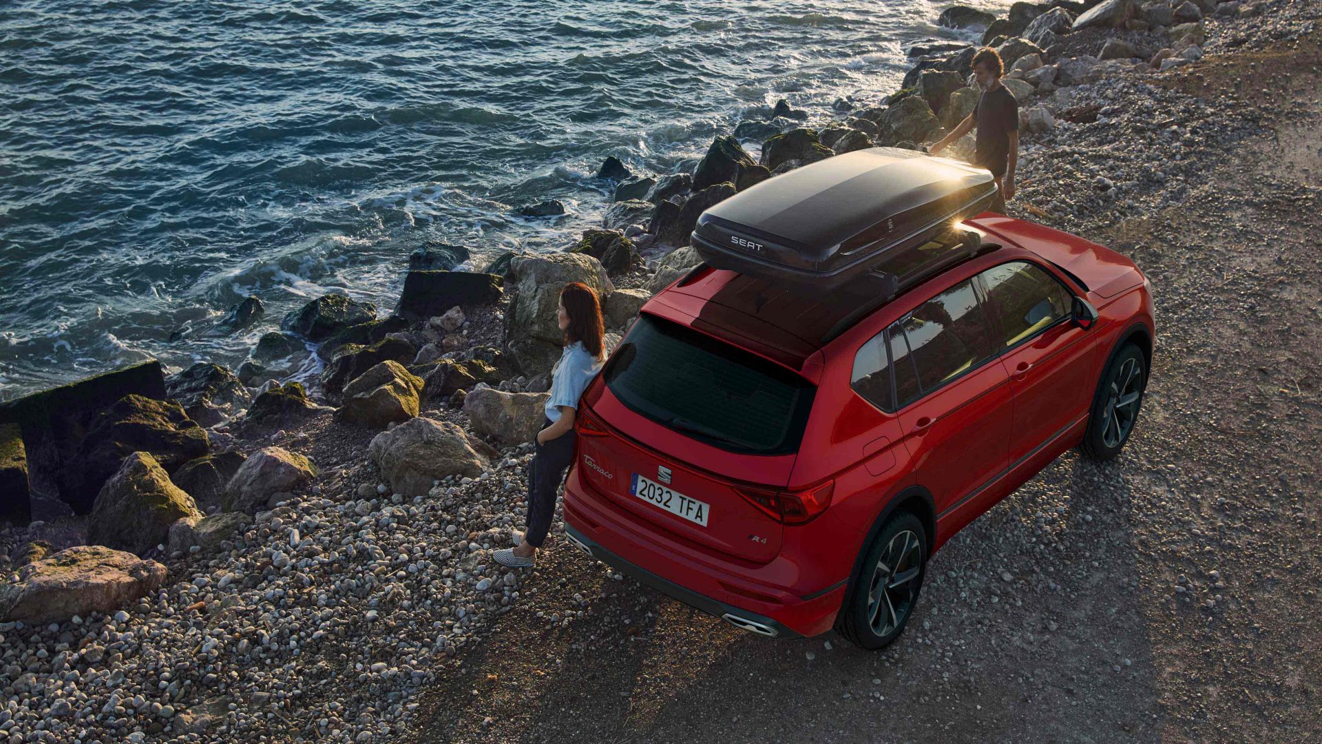 SEAT Tarraco mit Dachbox am Meer mit Paar daneben