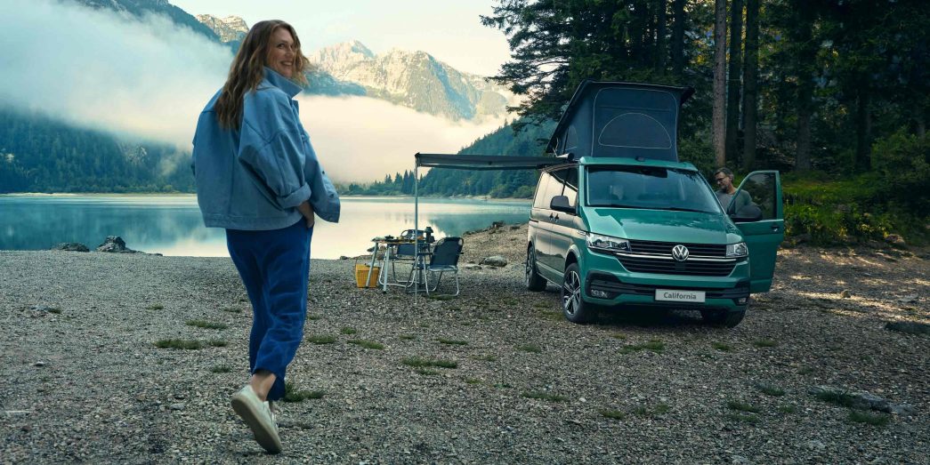 Green VW California front view next to a lake