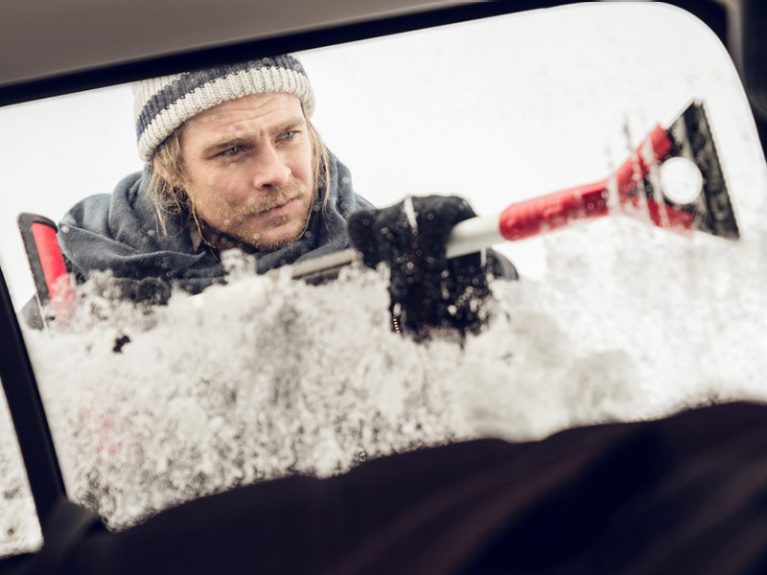 Un homme gratte la glace sur le pare-brise 